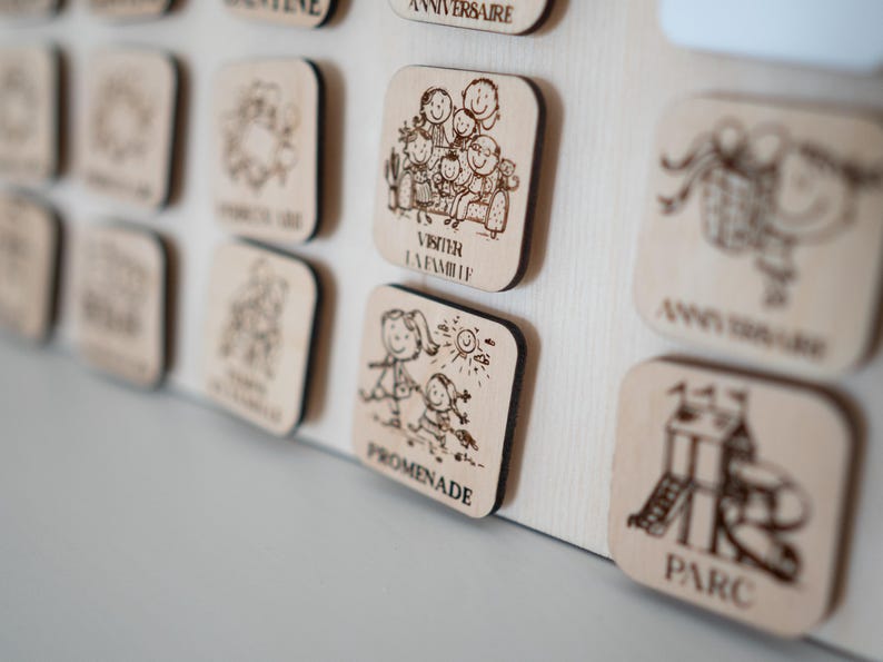 May include: Wooden square plaques with etched illustrations and text. The plaques depict family activities, including a family gathering, a walk, and a playground. The text includes the words "VISITER LA FAMILLE", "PROMENADE", and "PARC".