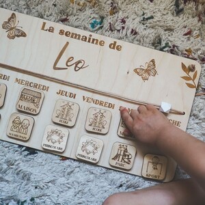 Pu&ograve; includere: Pannello settimanale in legno con il testo "La semaine de Leo" in alto. Il pannello ha una corda con una perla bianca che pu&ograve; essere spostata per indicare il giorno della settimana. Il pannello ha immagini di attivit&agrave; per ogni giorno della settimana, tra cui casa, scuola, parco e sport.