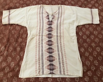 May include: A white tunic with a geometric pattern in shades of pink and purple. The tunic has a V-neck and short sleeves.