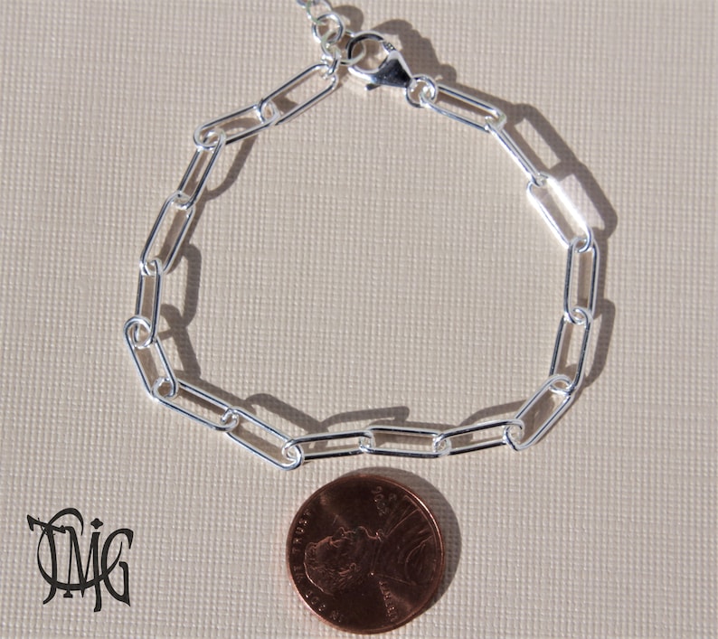 May include: A silver chain bracelet with a lobster clasp. The bracelet is about the size of a UK penny.