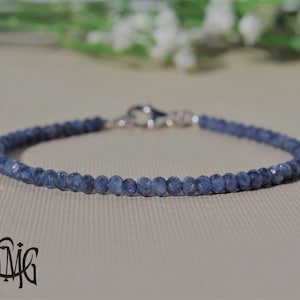 Könnte beinhalten: Ein zartes Armband aus kleinen, facettierten dunkelblauen Saphirperlen, die in einem durchgehenden kreisförmigen Strang angeordnet sind. Das Schmuckstück verfügt über einen polierten silberfarbenen Karabinerverschluss, der die Enden der Kette verbindet.