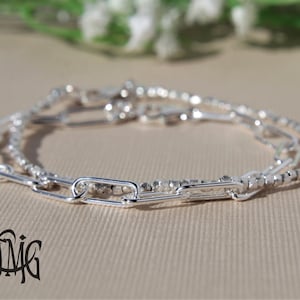 May include: A silver bracelet featuring three different chain styles. The bracelet includes a delicate beaded chain, a thicker chain with oval links, and a chain with small, square links.