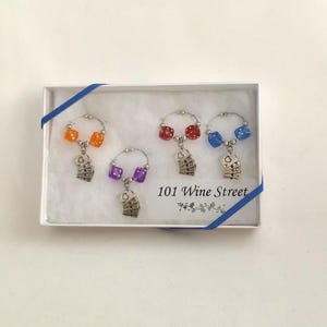 May include: Set of four wine glass charms in a white box with blue ribbon. Each charm features a silver playing card charm and a dice charm in orange, red, purple, and blue.