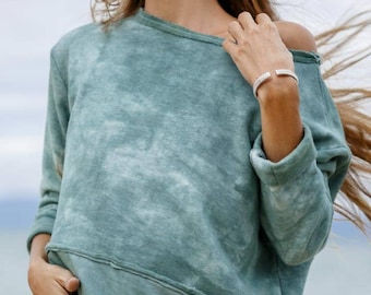 May include: A teal blue tie-dye sweatshirt with long sleeves and a relaxed fit. The sweatshirt has a distressed look and a small gold logo on the bottom left side.