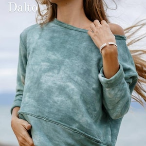 May include: A teal blue tie-dye sweatshirt with long sleeves and a relaxed fit. The sweatshirt has a distressed look and a small gold logo on the bottom left side.
