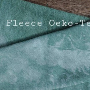 May include: A close-up of a soft, teal-coloured bamboo fleece fabric. The fabric has a subtle tie-dye pattern and the text "Bamboo Fleece Oeko-Tex" is visible in the top left corner.
