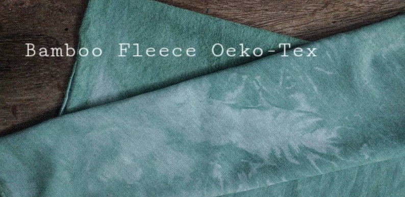 May include: A close-up of a soft, teal-coloured bamboo fleece fabric. The fabric has a subtle tie-dye pattern and the text "Bamboo Fleece Oeko-Tex" is visible in the top left corner.