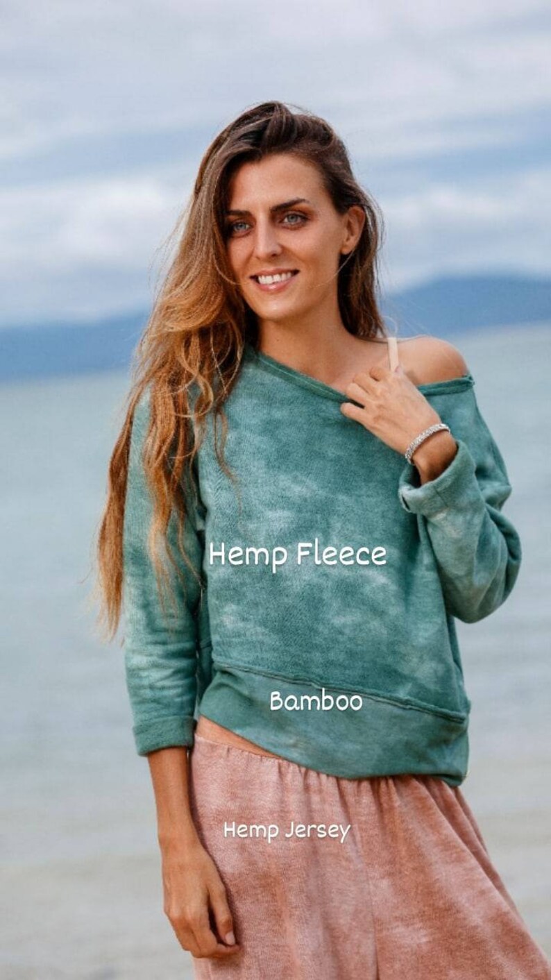 May include: A woman wearing a green tie-dye hemp fleece sweatshirt with the text "Hemp Fleece" and "Bamboo" printed on it. She is also wearing a pair of pink hemp jersey trousers with the text "Hemp Jersey" printed on them.