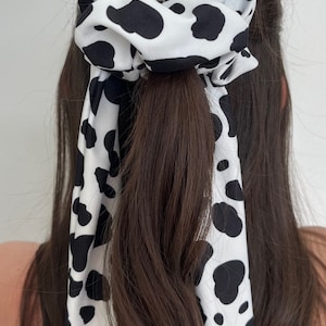 May include: A white and black cow print scrunchie with a long matching ribbon tail.