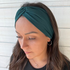 May include: A dark green knotted headband made of soft fabric. The headband is worn by a person with long brown hair.