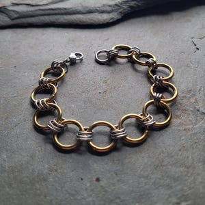 May include: A gold and silver-toned bracelet featuring a series of interconnected circular links. The gold-colored rings are interspersed with silver-colored wire wraps, creating a contrasting design. The bracelet has a silver clasp.