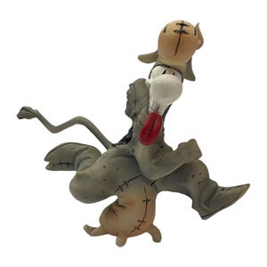 May include: A stylized figurine of a grey, stitched-together creature with a long, thin tail, a large white snout, and a prominent red tongue. The figure is posed in a dynamic, leaping motion with visible black stitch marks across its body.