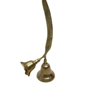 May include: A gold-colored brass bell with a feather-shaped handle. The bell is a decorative item and has a traditional design.