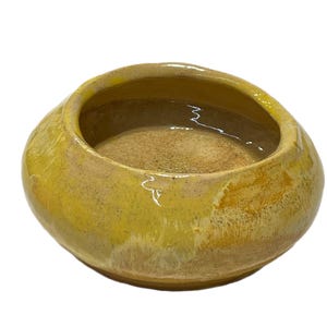 May include: A handmade, ceramic bowl with a wide, shallow design. The bowl features a blend of yellow and brown hues, with a glossy finish. The interior has a textured appearance, and the rim is slightly uneven. This decorative bowl is suitable for various uses.