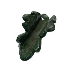 May include: A dark green ceramic dish shaped like an oak leaf with a glossy, mottled finish. The object features a central elongated depression with raised, wavy edges that mimic the natural, irregular lobes and curves of a botanical leaf form.