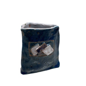May include: A small, blue ceramic vase with a white glaze and a geometric design. The vase has a rectangular shape and a slightly uneven surface.