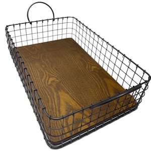 May include: A rectangular wire basket featuring a dark metal grid frame and a solid wooden base with a visible brown wood grain pattern. The basket includes a single arched metal handle attached to one of the shorter sides of the frame.