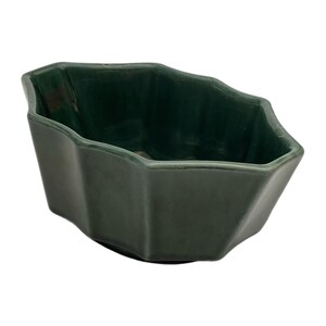 May include: A dark forest green ceramic bowl with a faceted, multi-sided geometric rim and a smooth, glossy finish. The vessel features a deep interior and a wide, irregular hexagonal opening, showcasing a solid, uniform color throughout the piece.