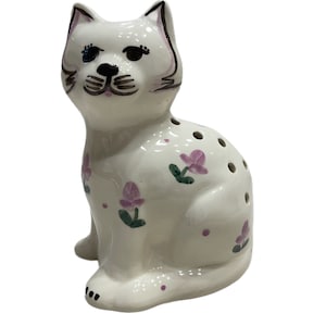 May include: White ceramic cat figurine with pink and green floral designs. The cat is sitting with its head tilted slightly to the side.
