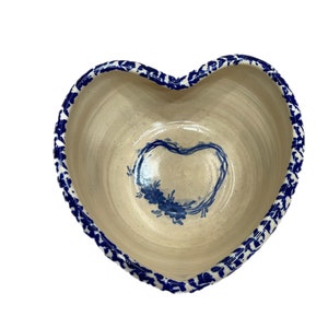 May include: A heart-shaped ceramic bowl with a blue and white floral design. The bowl has a scalloped edge and a white glaze.