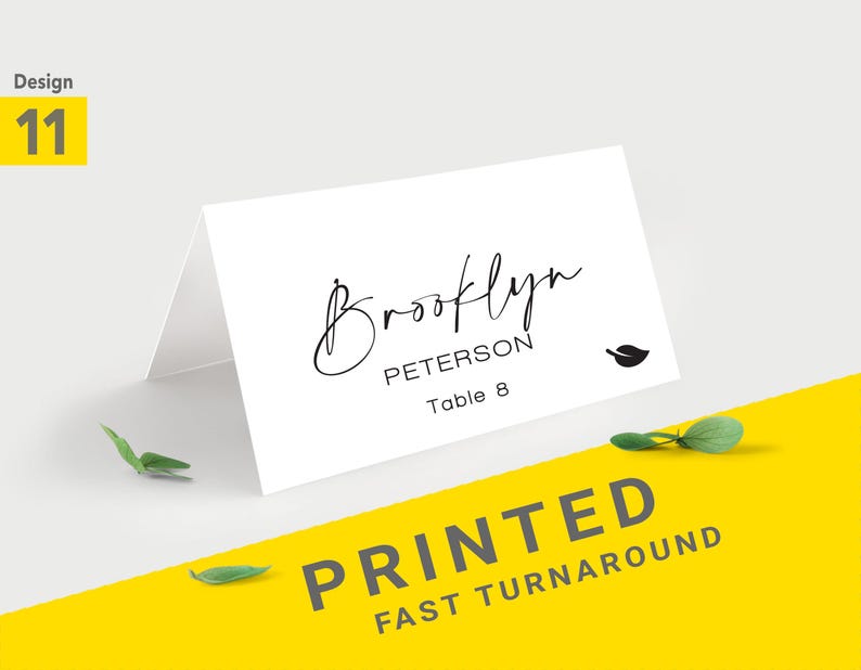 Pu&ograve; includere: Segnaposto bianco piegato con il nome "Brooklyn Peterson" in elegante scrittura nera. La carta include un'icona a forma di foglia e "Table 8". Le parole "PRINTED FAST TURNAROUND" sono stampate su sfondo giallo.