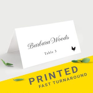 Pu&ograve; includere: Segnaposto piegato bianco con il nome "Barbara Woods" in elegante corsivo, numero del tavolo 3 e una piccola silhouette di pollo nero. Le parole "PRINTED FAST TURNAROUND" sono stampate su sfondo giallo.