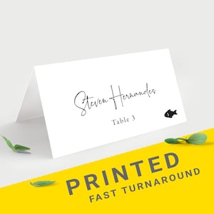 May include: White place card with the name "Steven Hernandez" in elegant script, table number 3, and a small fish illustration. The card is on a white surface with a yellow background that reads "PRINTED FAST TURNAROUND".