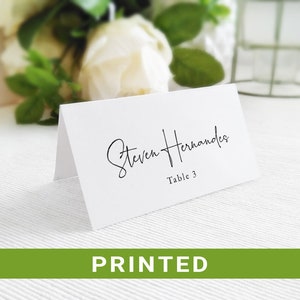 May include: White place card with black calligraphy text that reads "Steven Hernandez" and "Table 3".