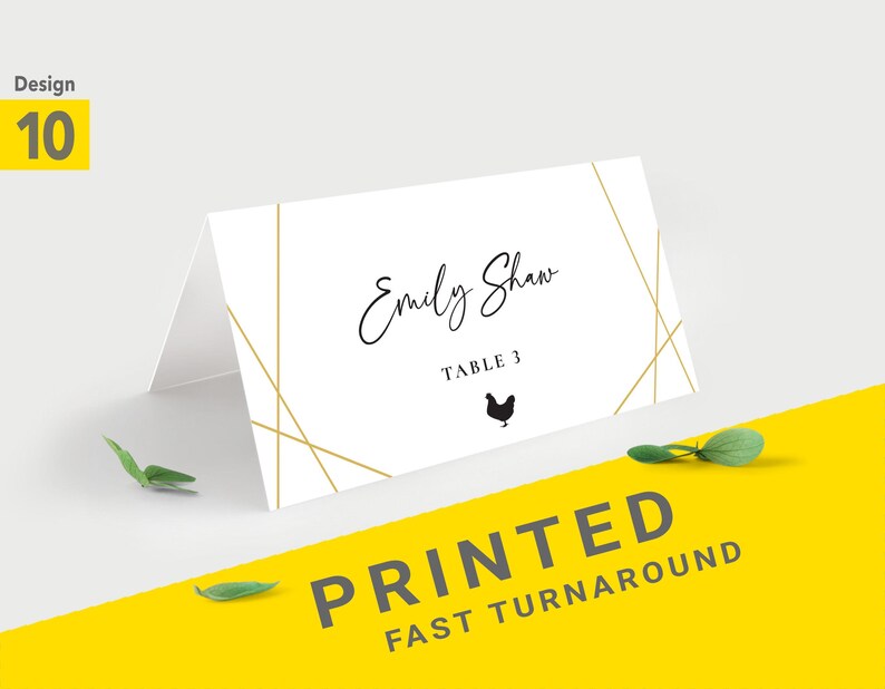 Pu&ograve; includere: Un segnaposto piegato bianco con linee geometriche dorate e il nome "Emily Shaw" in elegante corsivo. Sotto, si legge "Table 3" con una piccola silhouette di pollo. Le parole "PRINTED FAST TURNAROUND" sono stampate su sfondo giallo.