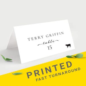 May include: A white place card with the name "TERRY GRIFFIN", table number 15, and a small cow silhouette. The words "PRINTED FAST TURNAROUND" are printed on a yellow background. The design is labeled "Design 1".