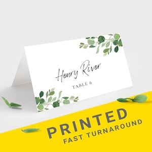 Pu&ograve; includere: Un segnaposto piegato bianco con il testo "Henry River" e "Table 6" in corsivo nero. Foglie e rami di eucalipto verde acquerello decorano gli angoli. Le parole "PRINTED FAST TURNAROUND" sono stampate su sfondo giallo.