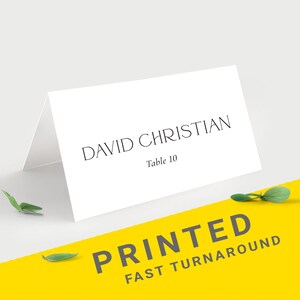 Pu&ograve; includere: Un segnaposto bianco piegato con il nome "DAVID CHRISTIAN" e "Table 10" stampati in nero. Il biglietto &egrave; su una superficie bianca con una striscia gialla angolata in basso che recita "PRINTED FAST TURNAROUND". Il design 15 &egrave; in un riquadro giallo.