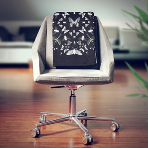 May include: A black office chair with a gray fabric seat and back. The chair has a chrome base with five wheels and a chrome armrest. A black throw blanket with a white butterfly pattern is draped over the back of the chair.