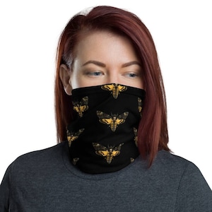 Puede incluir: Una máscara facial negra con un patrón repetido de polillas amarillas y negras. Las polillas tienen un diseño de calavera y huesos cruzados.
