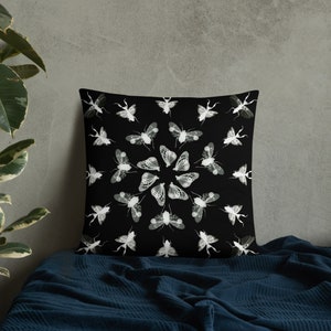 K&ouml;nnte beinhalten: Schwarzes und wei&szlig;es Kissen mit einem kreisf&ouml;rmigen Design aus Insekten und Motten. Das Kissen liegt auf einer blauen Decke.