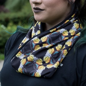 Puede incluir: Una bufanda infinita negra con un estampado de mariposa colorido. La bufanda está hecha de un tejido suave y elástico y es perfecta para añadir un toque de color a cualquier atuendo.
