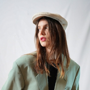 May include: A green and white checkered blazer with a single button closure. The blazer has a notched lapel and long sleeves. The person wearing the blazer is also wearing a light beige newsboy cap.