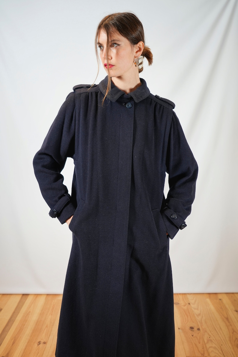 May include: A long, navy blue coat with a button closure and pockets. The coat has a classic, tailored style.
