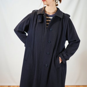 May include: A long navy blue coat with a button closure and pockets. The coat has a collar and a belt.