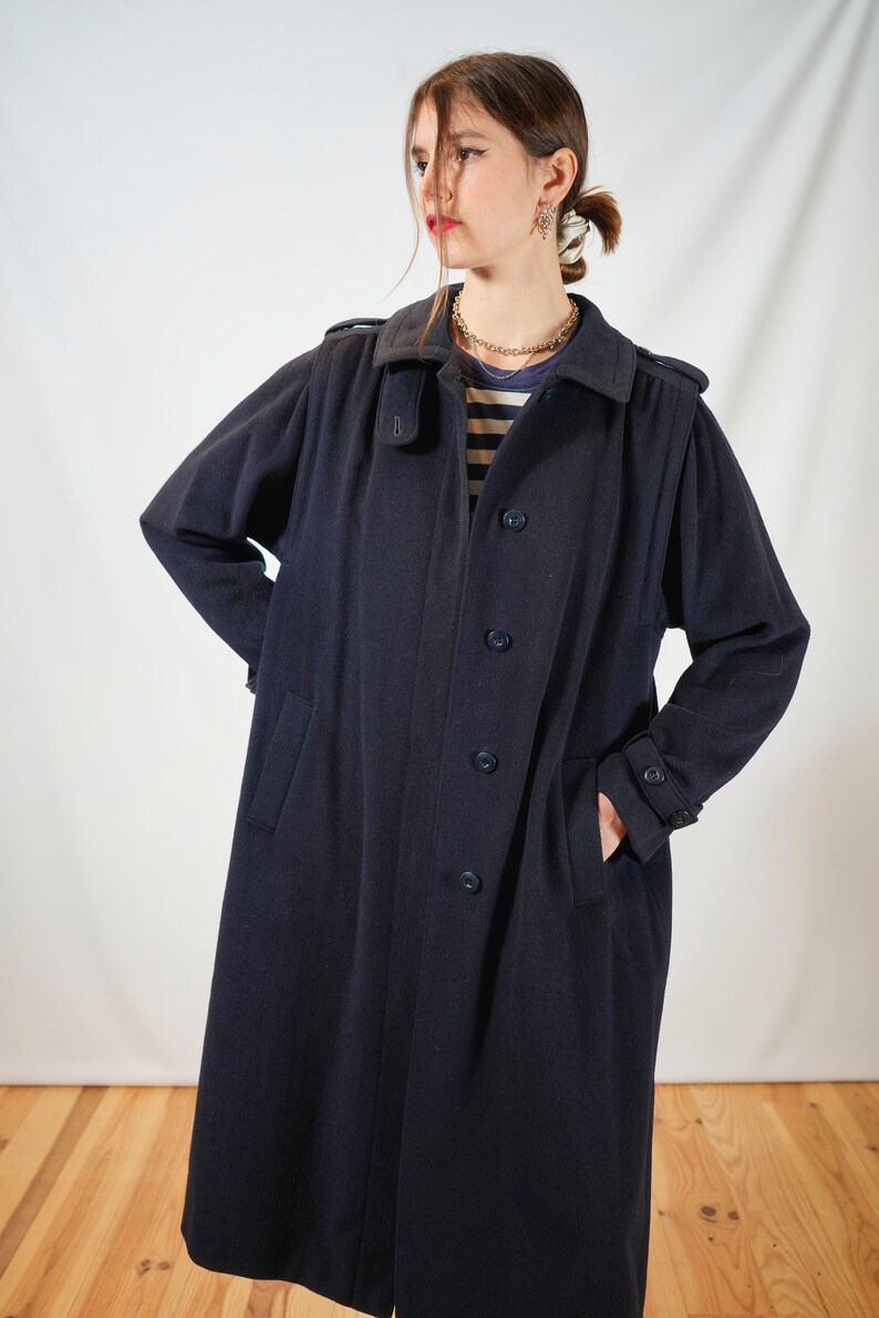 May include: A long navy blue coat with a button closure and pockets. The coat has a collar and a belt.