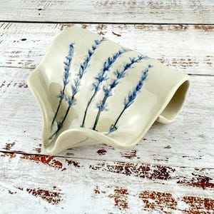 May include: A ceramic dish with a wavy edge and a lavender floral design. The dish is cream coloured with blue and green lavender flowers.
