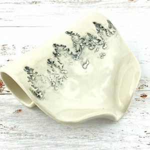 May include: A white ceramic soap dish with a wavy edge and a black and white tree design.