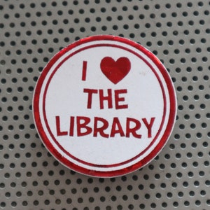 May include: A red and white button with a red heart and the text "I love the library".