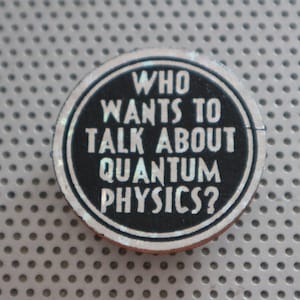May include: A black and white round button with the text "WHO WANTS TO TALK ABOUT QUANTUM PHYSICS?" in white letters.