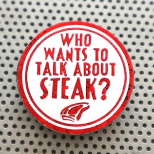 Puede incluir: Un botón redondo blanco con un borde rojo y el texto "WHO WANTS TO TALK ABOUT STEAK?" en letras rojas. Una silueta roja de un bistec se encuentra en la parte inferior del botón.