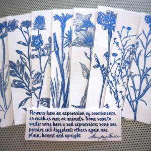 May include: A collection of white bookmarks with blue floral designs. Each bookmark displays a different botanical illustration, such as tulips and other wildflowers. A small card with text about flowers is included.