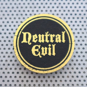 May include: A round, black and gold pin with the words "Neutral Evil" written in gold lettering.