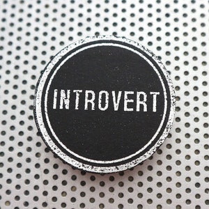 Puede incluir: Una pegatina redonda en blanco y negro con la palabra "INTROVERT" escrita en letras blancas sobre un fondo negro.