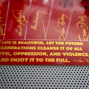 May include: Red rectangular sticker with gold lettering that reads "LIFE IS BEAUTIFUL. LET THE FUTURE GENERATIONS CLEANSE IT OF ALL EVIL, OPPRESSION, AND VIOLENCE, AND ENJOY IT TO THE FULL.  Len Trotsky"