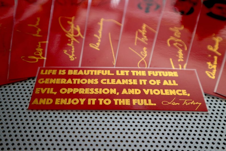 May include: Red rectangular sticker with gold lettering that reads "LIFE IS BEAUTIFUL. LET THE FUTURE GENERATIONS CLEANSE IT OF ALL EVIL, OPPRESSION, AND VIOLENCE, AND ENJOY IT TO THE FULL.  Len Trotsky"